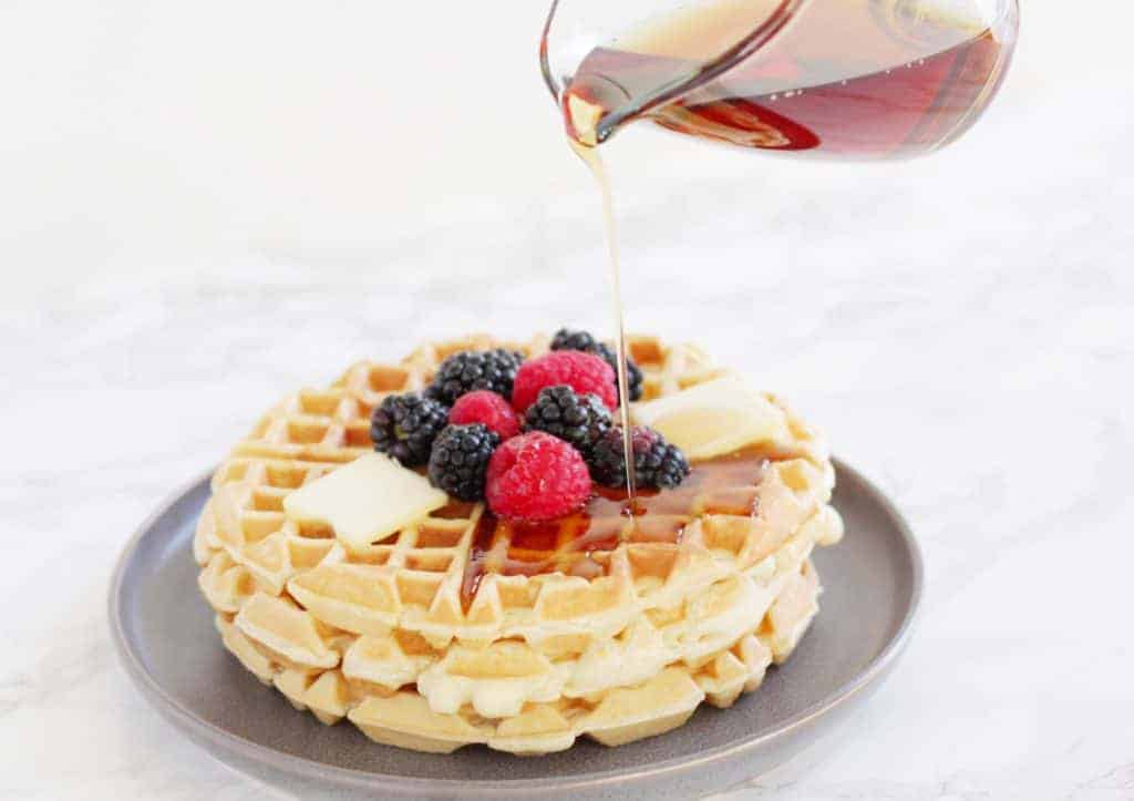 Close-up of fruit covered waffles, syrup being poured