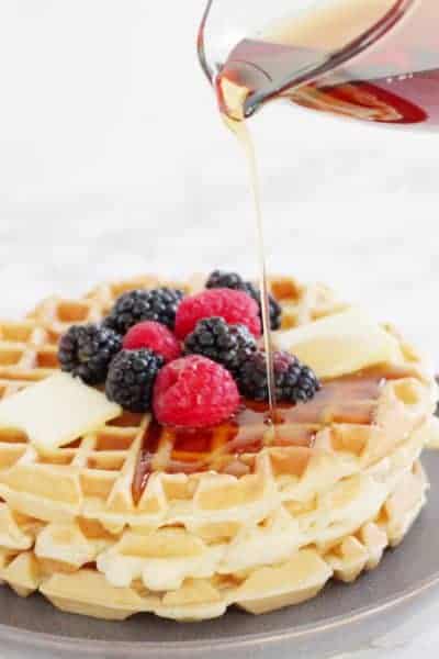 Syrup being poured on fluffy waffles topped with fruit