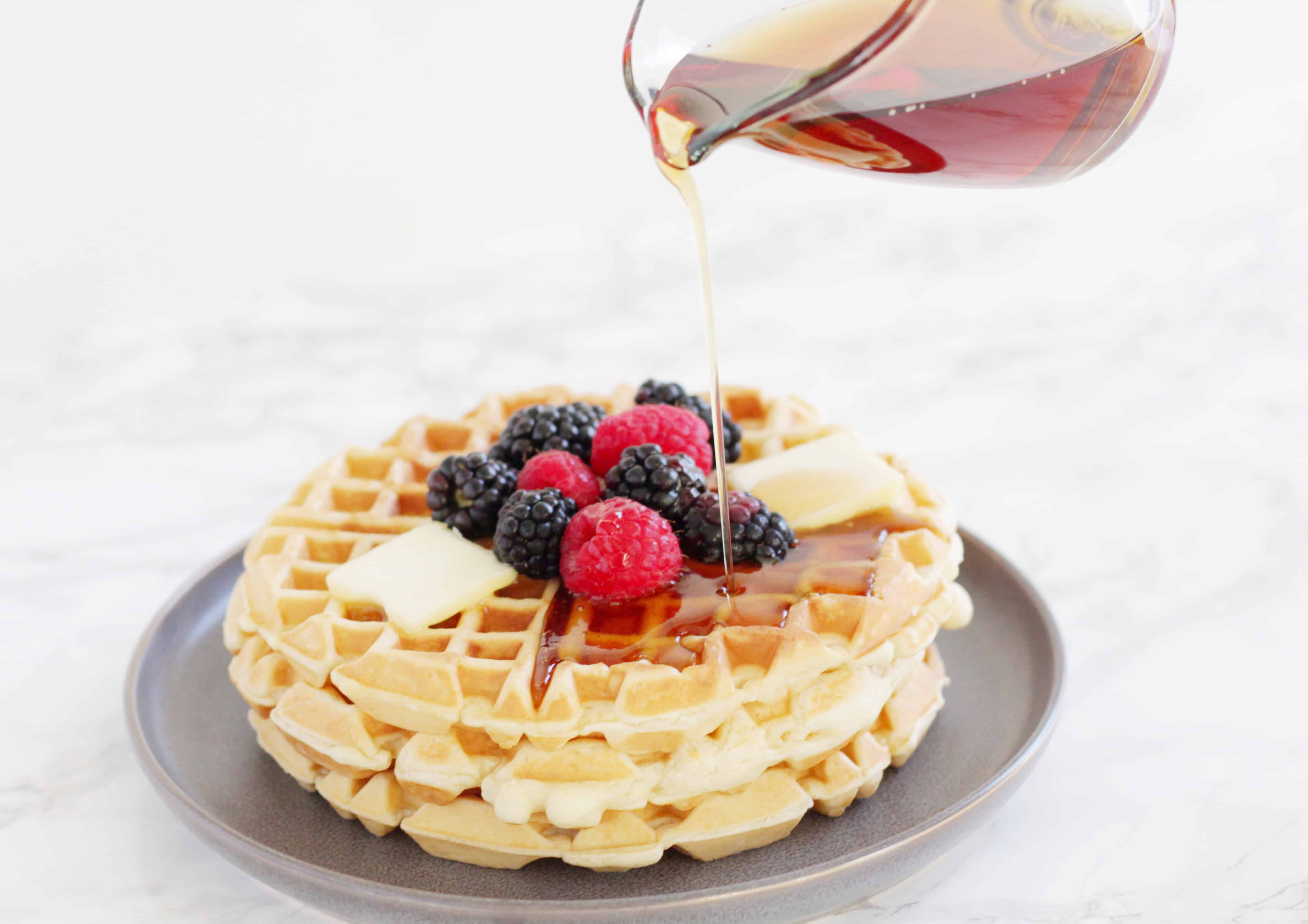 Syrup being poured on fluffy waffles topped with fruit