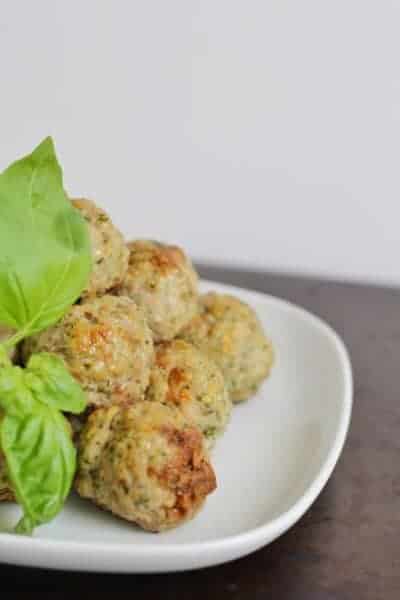 A pile of baked meatballs with some basil