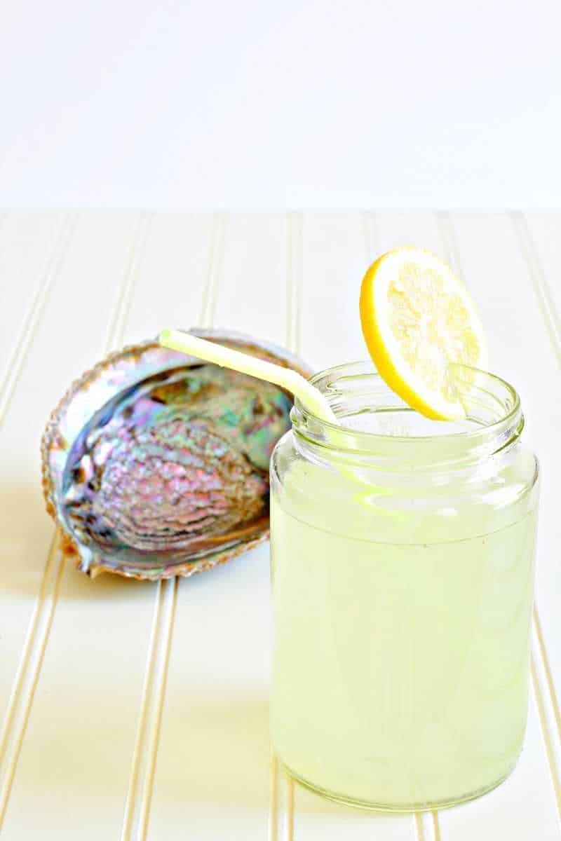 Yellow lemonade in a glass next to a shell