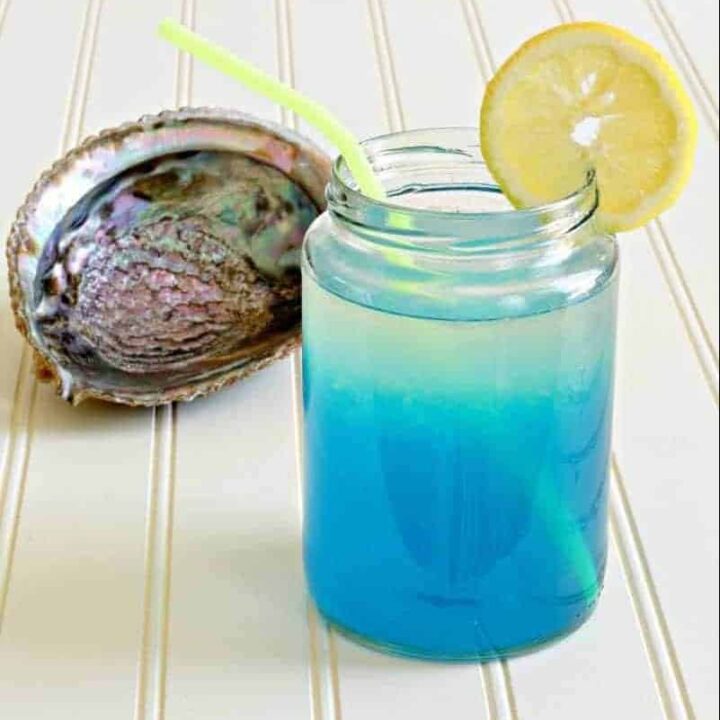 Blue and yellow mermaid lemonade in a glass next to a shell