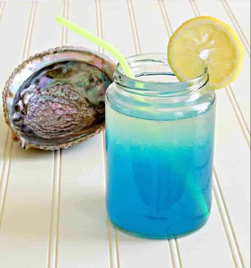 Blue and yellow mermaid lemonade in a glass next to a shell