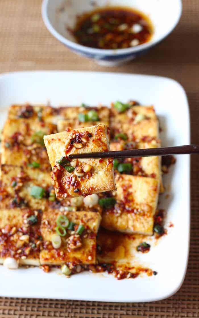 A chopstick holding a pan fried spicy tofu square