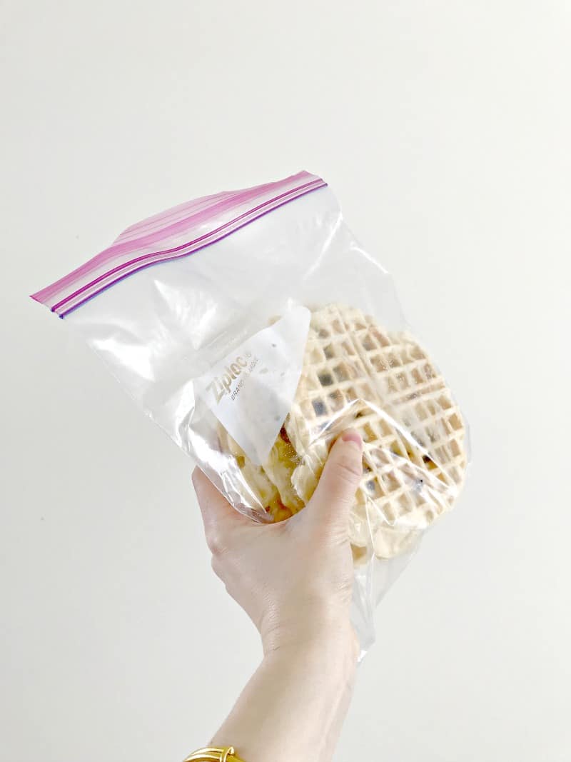 A hand holding frozen waffles in a bag