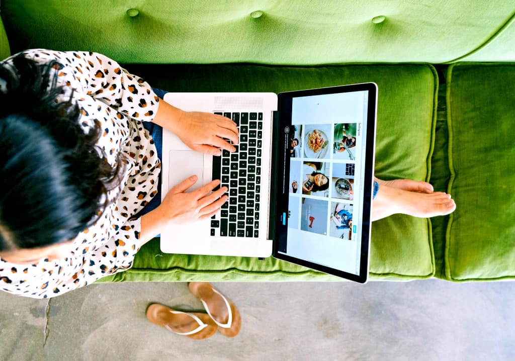 A woman working on her virtual assistant side hustle at home on her green couch.