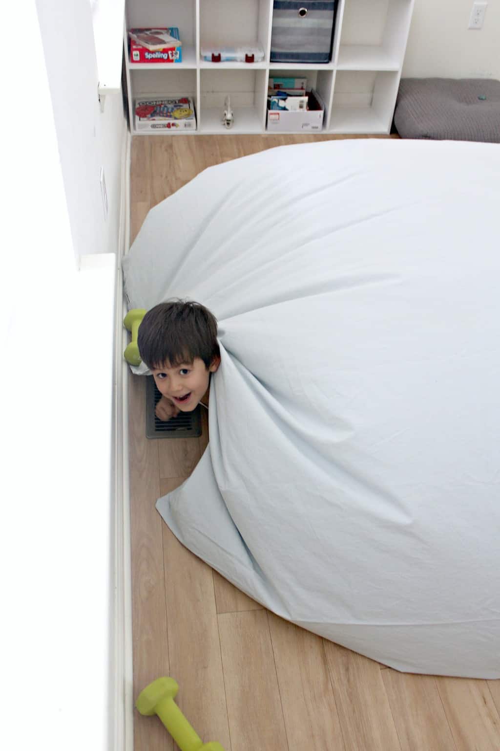 A boy peeking out from under an air fort.