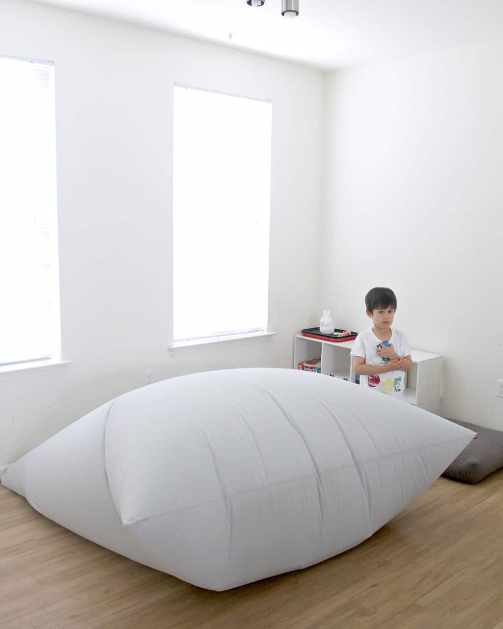 A boy standing next to a large air fort diy tent.