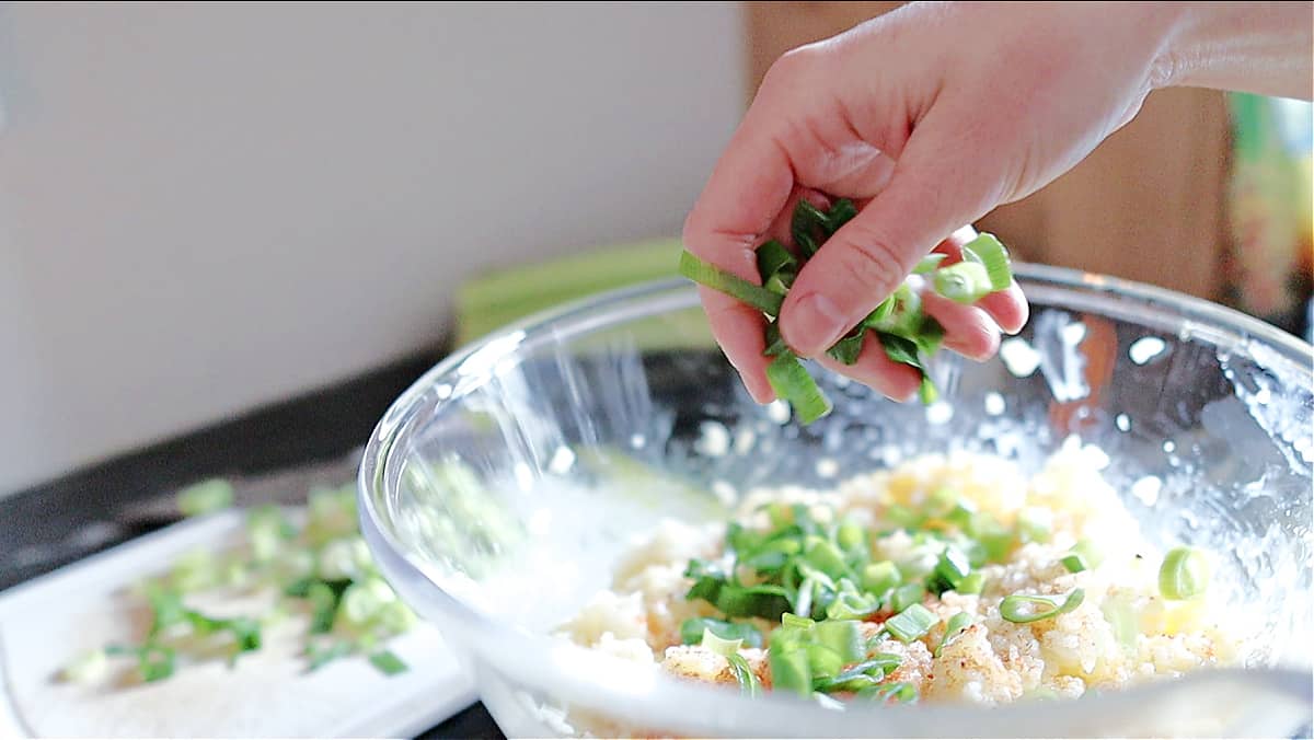 A woman's hand adding green onions to a cheesy rice pancake recipe
