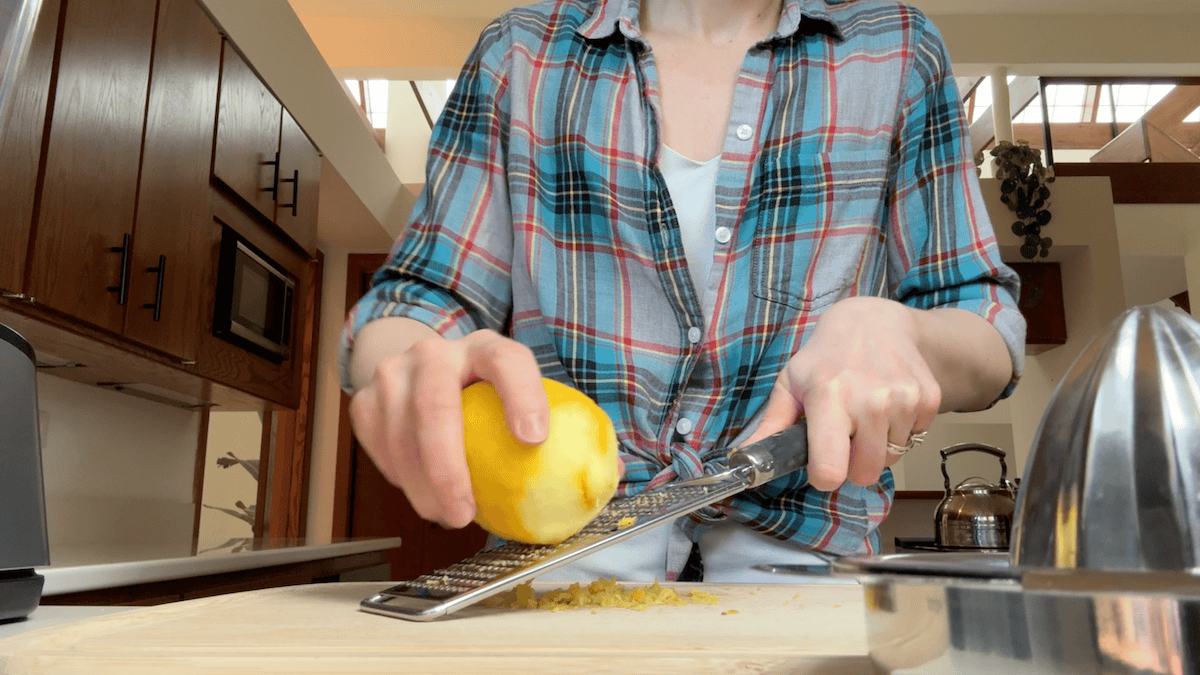 Woman in plaid shirt grating lemon and teaching how to make protein cheesecake